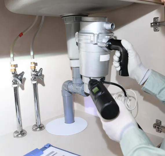 Plumber inspecting a garbage disposal unit under a kitchen sink, highlighting plumbing maintenance and repair services.
