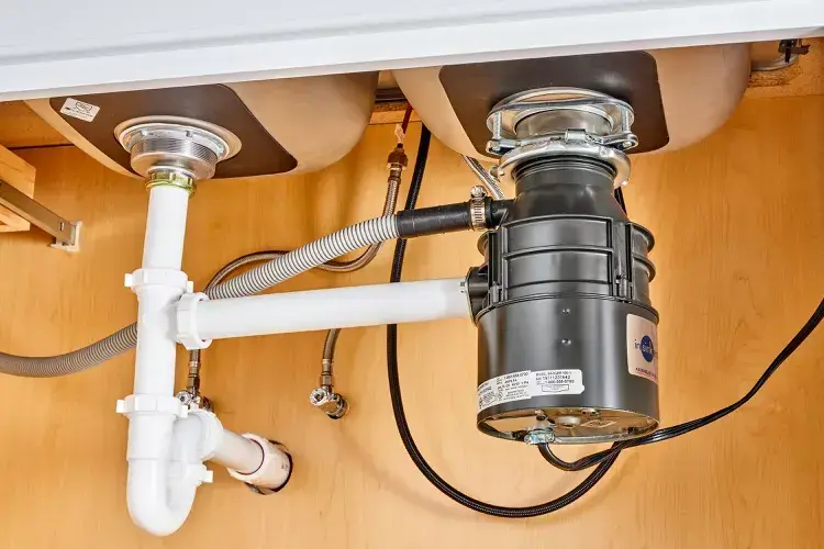 Garbage disposal unit installed under kitchen sink with plumbing connections, showcasing efficient food waste management for improved kitchen cleanup.